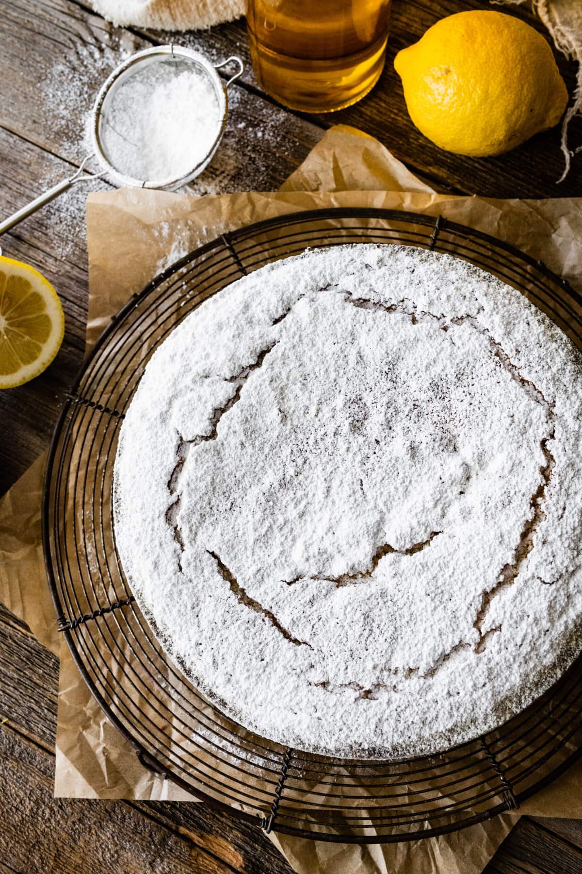 baked best olive oil cake with powdered sugar on a cooling rack with lemons around and bottle of olive oil.