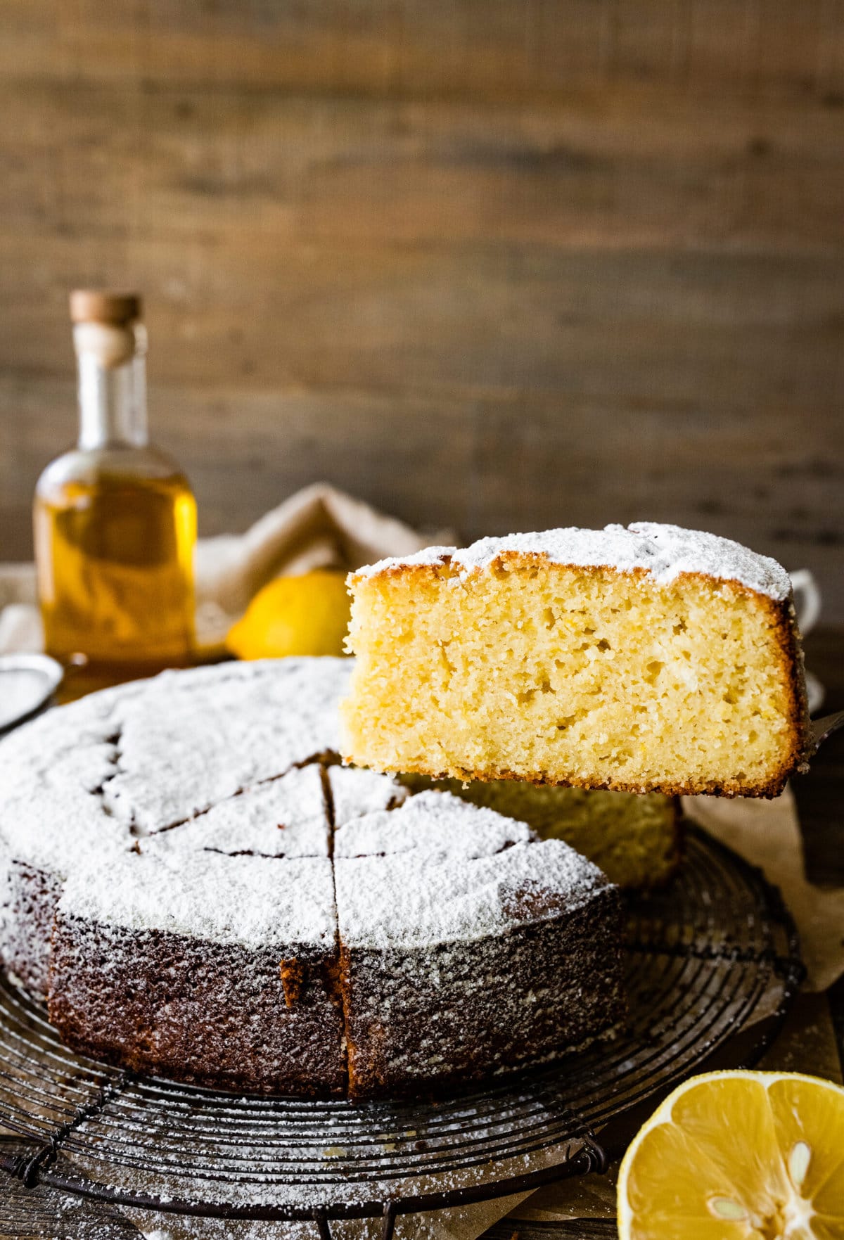 baked best olive oil cake with powdered sugar on top. Cake cut into slices. One slice is taken out with a cake server. 