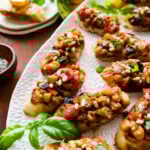 caponata recipe on grilled bread or crostini. on a platter with basil leaves and pine nuts as decoration.