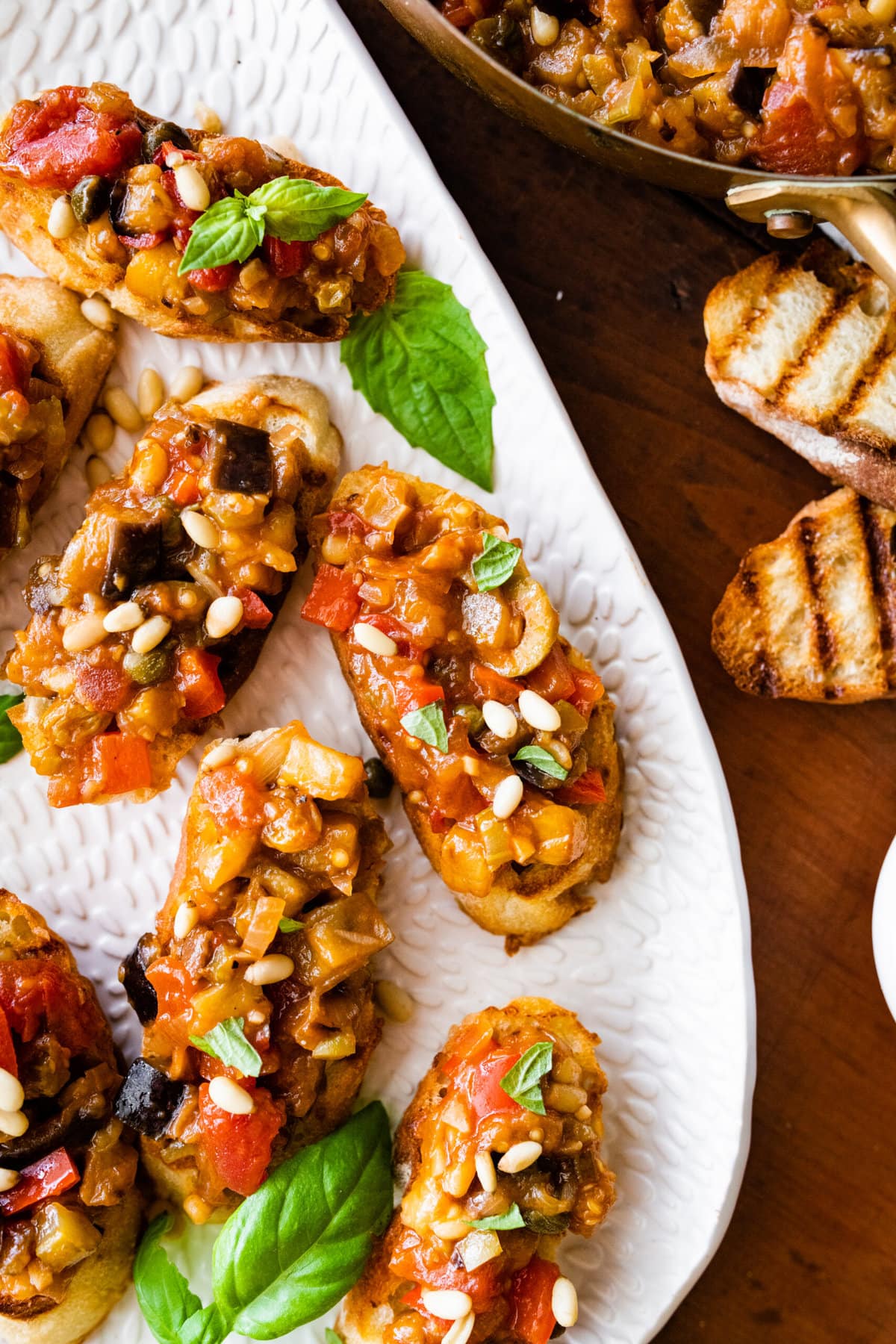 caponata recipe on grilled bread or crostini. on a platter with basil leaves and pine nuts as decoration.