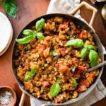 caponata in a pan with fresh basil as garnish. wood spoon in the pan.