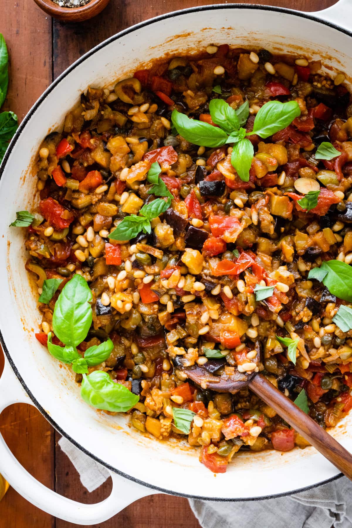 caponata in a pan with fresh basil as garnish. wood spoon in the pan. 