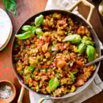 caponata in a pan with fresh basil as garnish. wood spoon in the pan.