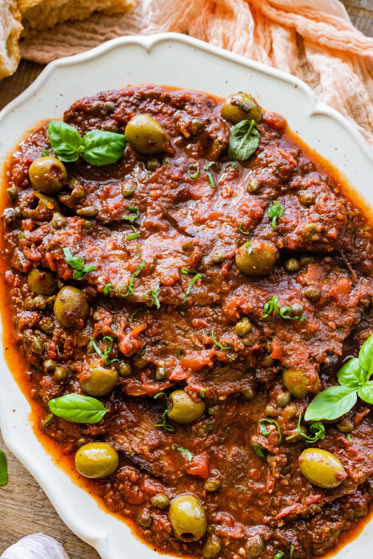 close up ofplatted steak pizzaiola recipe in a white dish with fresh basil as a garnish.