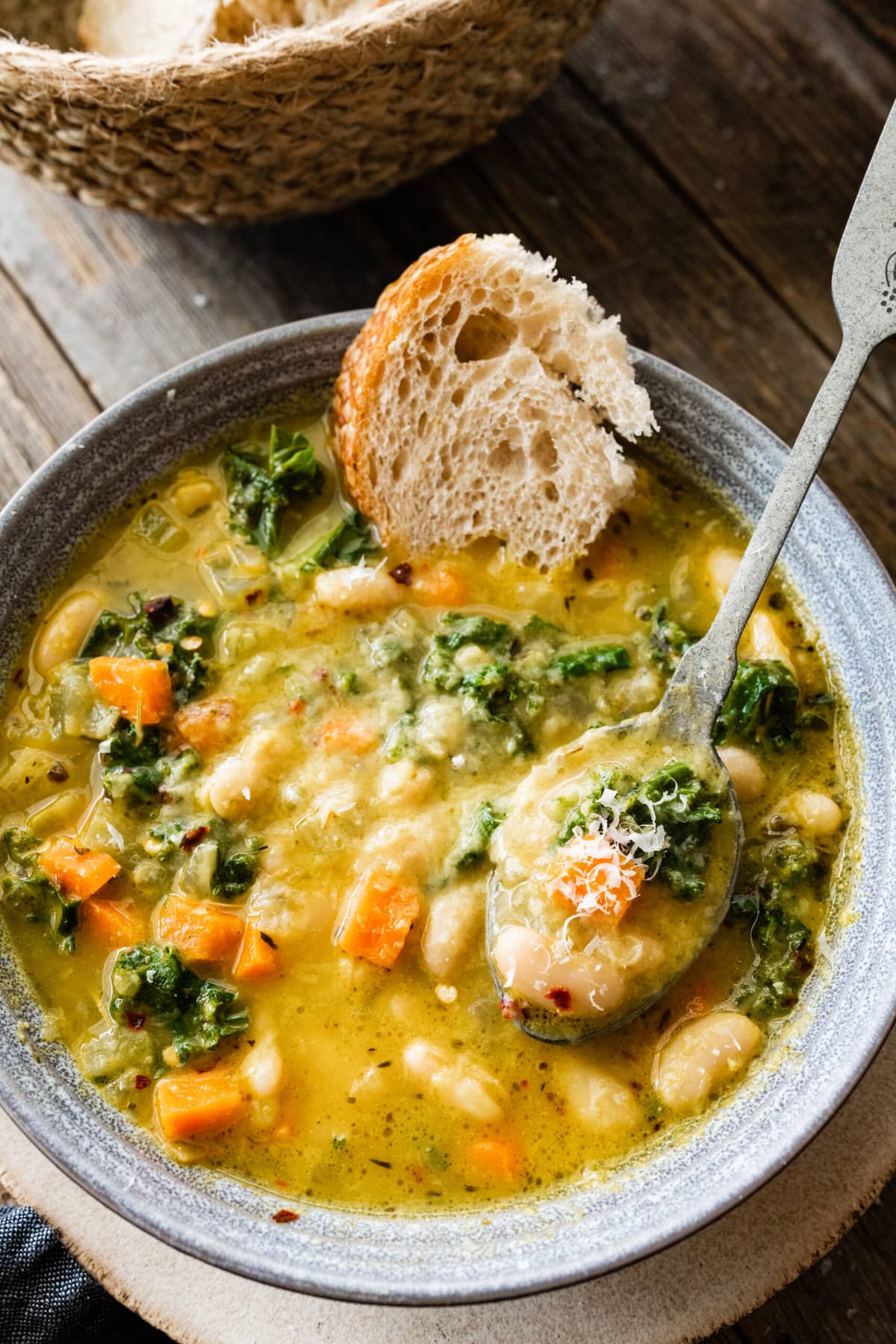 spoon in bowl of the tuscan white bean soup with a chunk of bread in it.