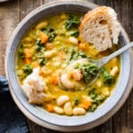 spoon in bowl of the tuscan white bean soup with a chunk of bread in it.