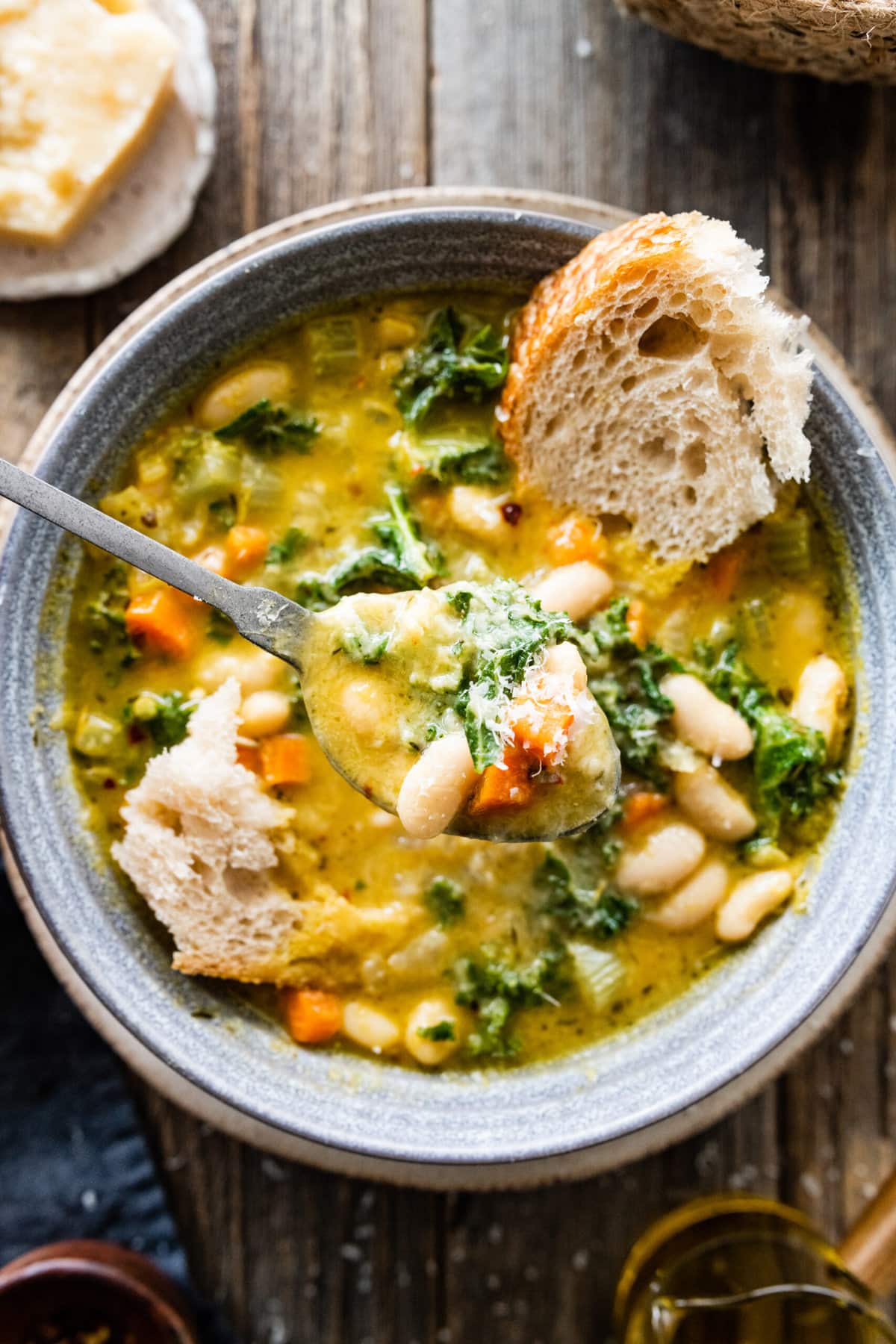 spoon in bowl of the tuscan white bean soup with a chunk of bread in it.
