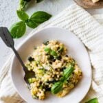 finished Fregola Sarda Pasta Recipe with Zucchini and Cheese in pan. Up close shot on a white plate with a fork.