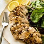 baked chicken on a plate with a side salad. Chicken cut into slices and sauce drizzled on the top.