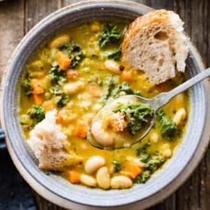 spoon in bowl of the tuscan white bean soup with a chunk of bread in it.