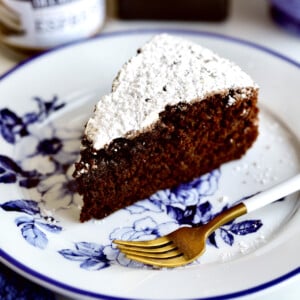 Slice of chocolate olive oil cake on a blue and white floral plate with a fork.