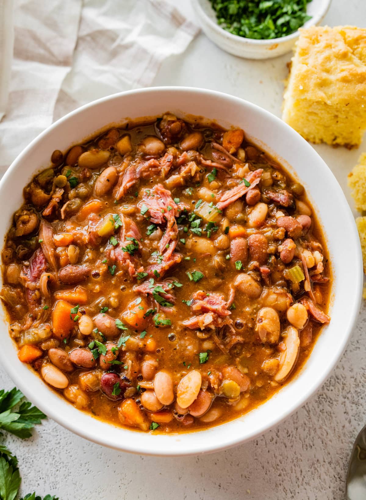 15 bean soup mix recipe in a white bowl with slices of cornbread on the side.