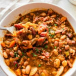15 bean soup mix recipe in a white bowl with slices of cornbread on the side. spoon in bowl taking a bite of the soup.