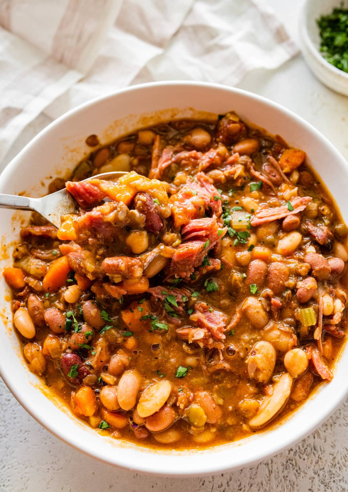 15 bean soup mix recipe in a white bowl with slices of cornbread on the side. spoon in bowl taking a bite of the soup.