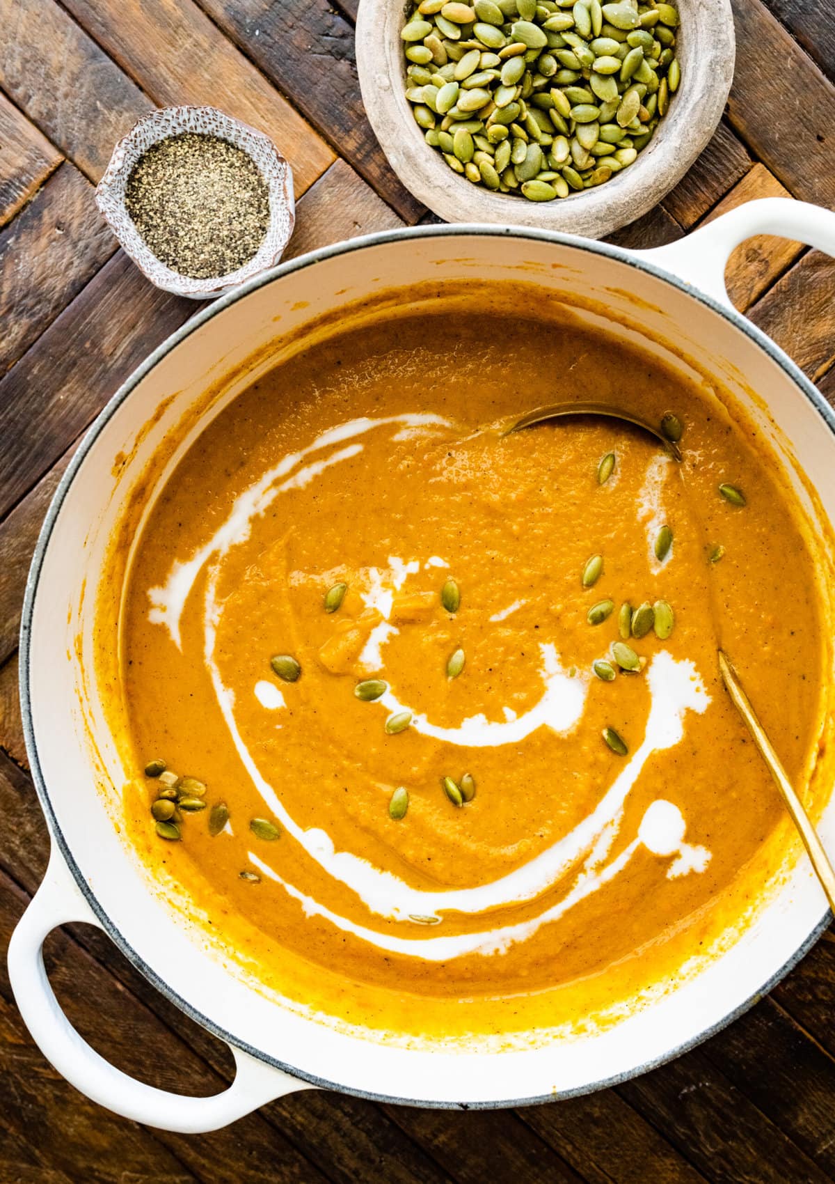 How to make Copycat Panera Autumn Squash Soup Recipe Step by Step Photos- blended soup in pot with swirl of cream and pumpkin seeds. Ladle in pot of soup.
