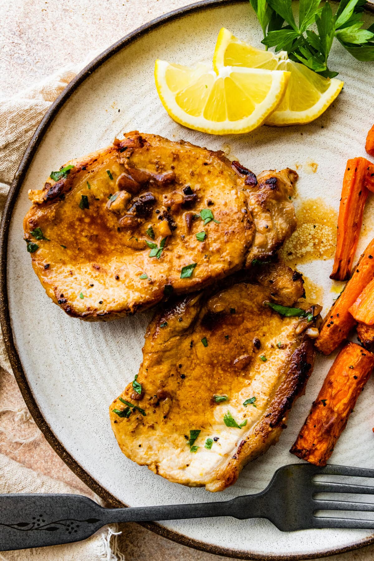 two juicy thin pork chops on a plate wit cooked carrots as a side dish.