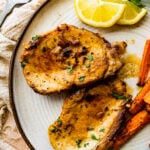 two juicy thin pork chops on a plate wit cooked carrots as a side dish.