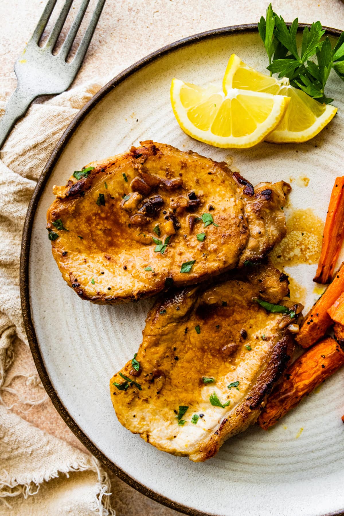 two juicy thin pork chops on a plate wit cooked carrots as a side dish.