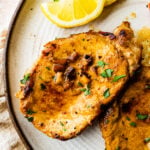 two juicy thin pork chops on a plate wit cooked carrots as a side dish.
