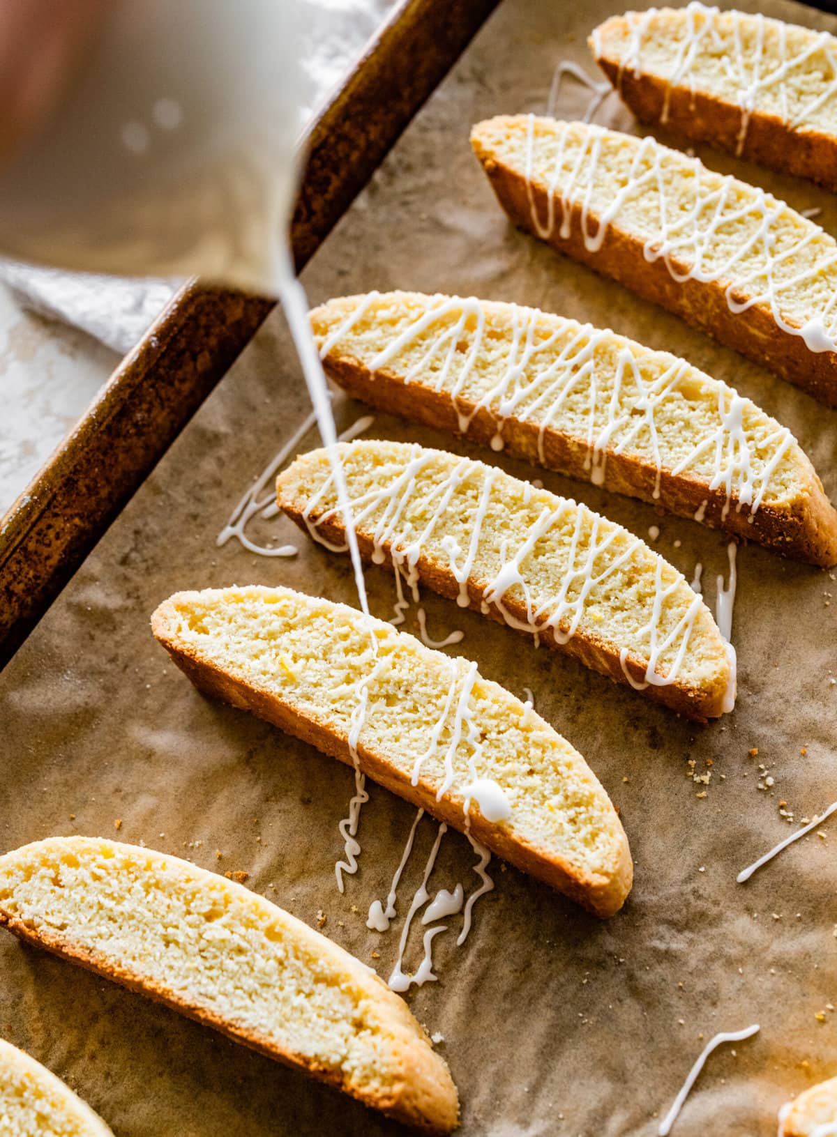 How to make Best Lemon Biscotti Recipe Step-by-Step: drizzling the glaze of the biscotti on the parchment paper.