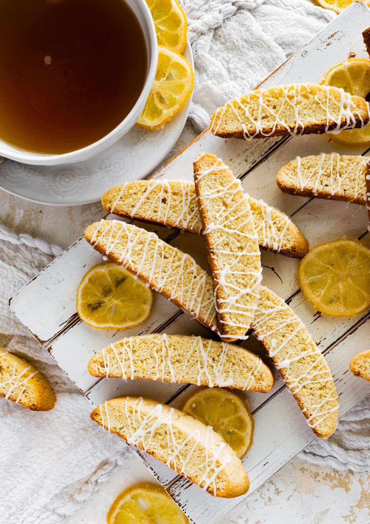 beautiful lemon biscotti on white background with lemon slices around it and a cup of tea.