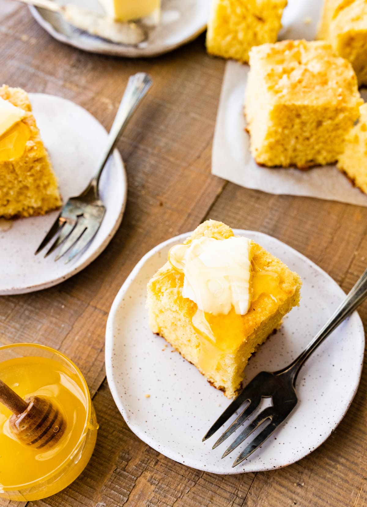 several slices of sweet cornbread on a plate with butter and honey on top.