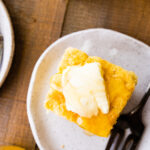 several slices of sweet cornbread on a plate with butter and honey on top. Black fork on the plate.