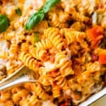 Cheesy Baked Rotini pasta after it is baked melty cheese on top with a few basil leaves. Spatula lifting up with a cheese pull.