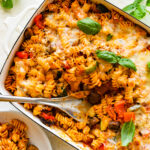 Cheesy Baked Rotini pasta after it is baked melty cheese on top with a few basil leaves. Spatula lifting up with a cheese pull.