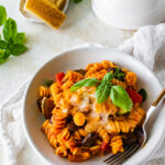 bowl of cheesy baked rotini pasta with vegetables with fork in it. pArmigiano cheese on the side.