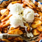 Spoon in a bowl of baked cinnamon apples topped with ice cream.