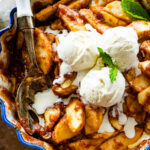 Easy baked cinnamon apples in a pie plate with blue rim. Vanilla Ice cream in the middle of apples with serving spoon.