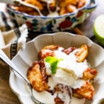 easy baked cinnamon apples in a white fluted bowl. Melty ice cream and spoon.