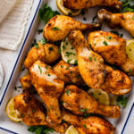 chicken drumsticks in a white serving dish with lemon and parsley as garnish.