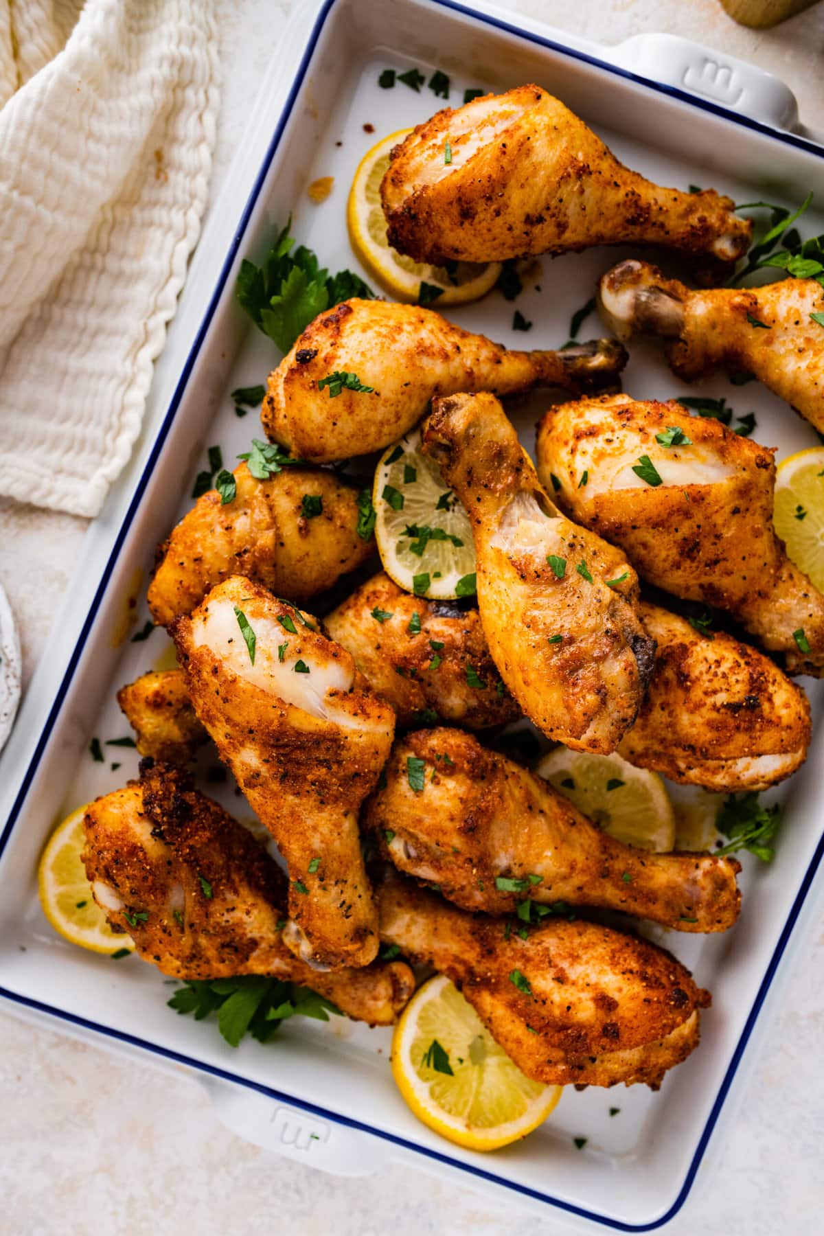 chicken drumsticks in a white serving dish with lemon and parsley as garnish. 