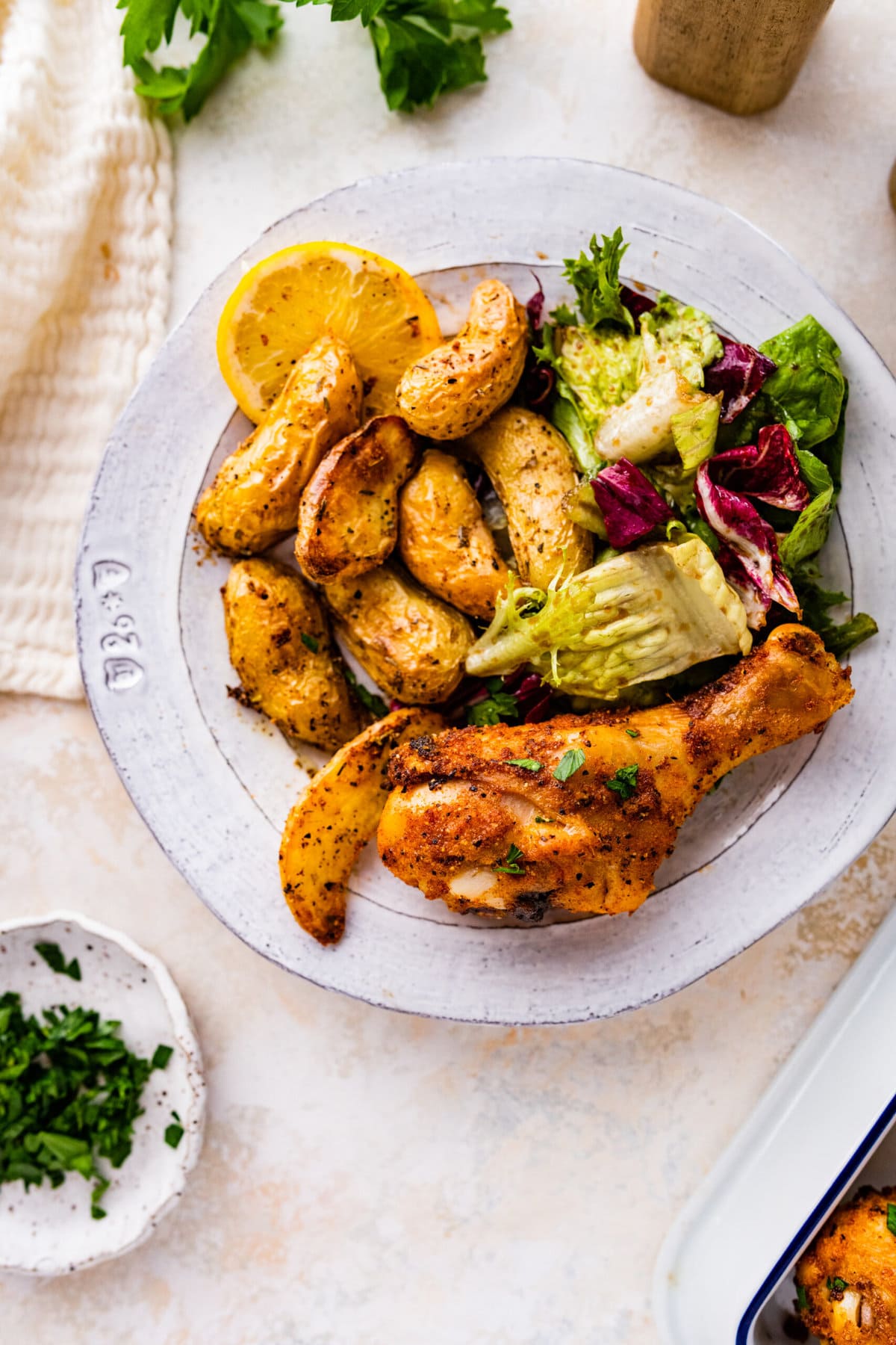 white plate with baked chicken drumstick with potatoes and salad.
