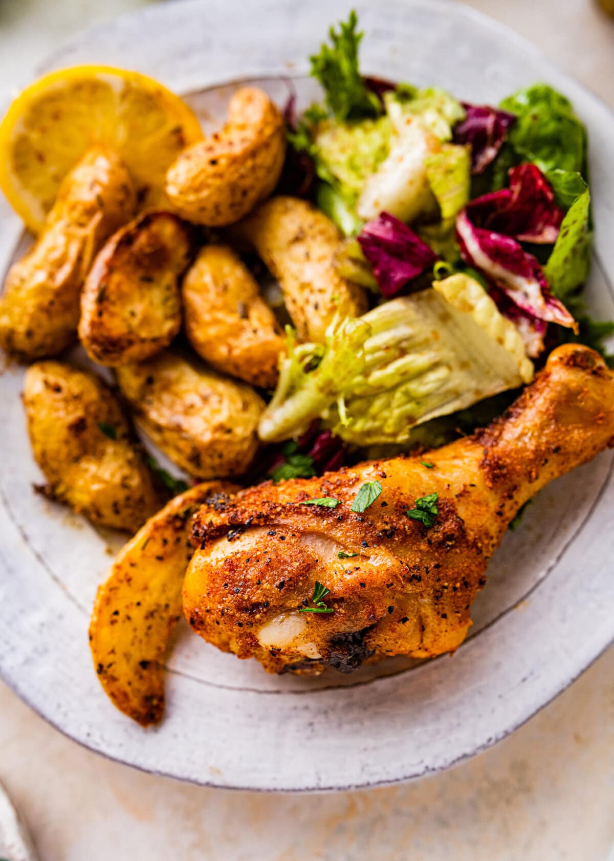 white plate with baked chicken drumstick with potatoes and salad.