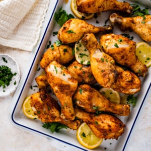 chicken drumsticks in a white serving dish with lemon and parsley as garnish.