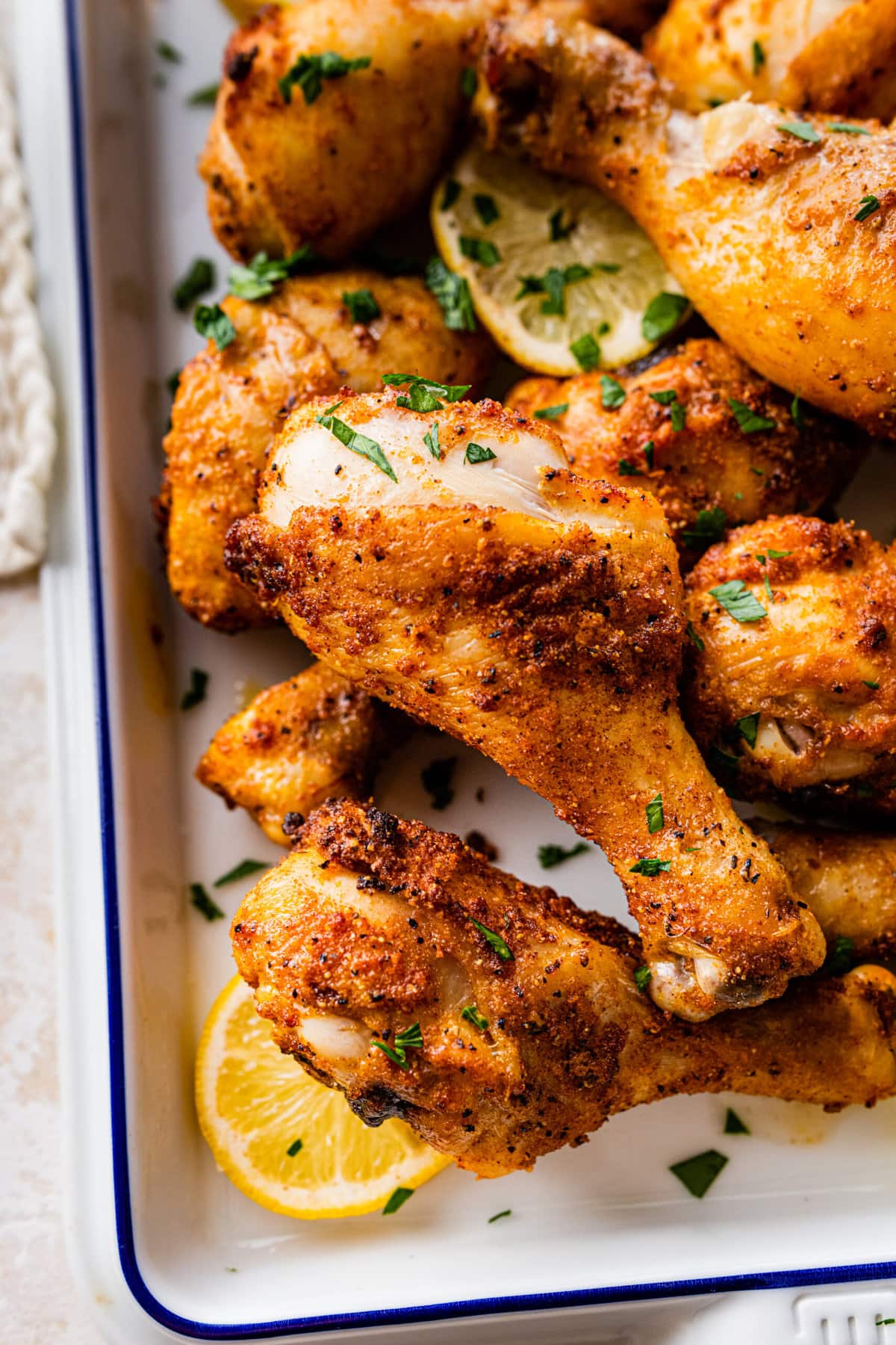 chicken drumsticks in a white serving dish with lemon and parsley as garnish. Close up shot.