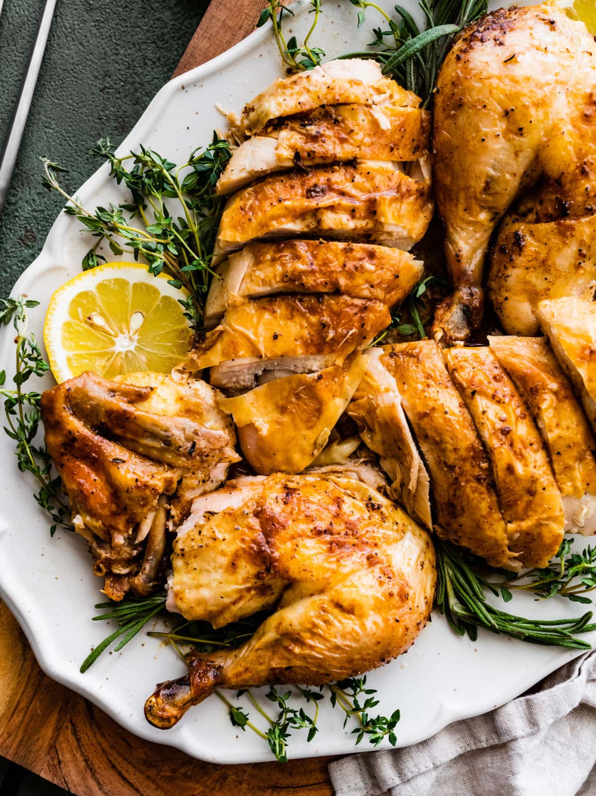 whole chicken recipe perfect and juicy. finished chicken cut and on a pretty platter with herbs and lemons as decoration.