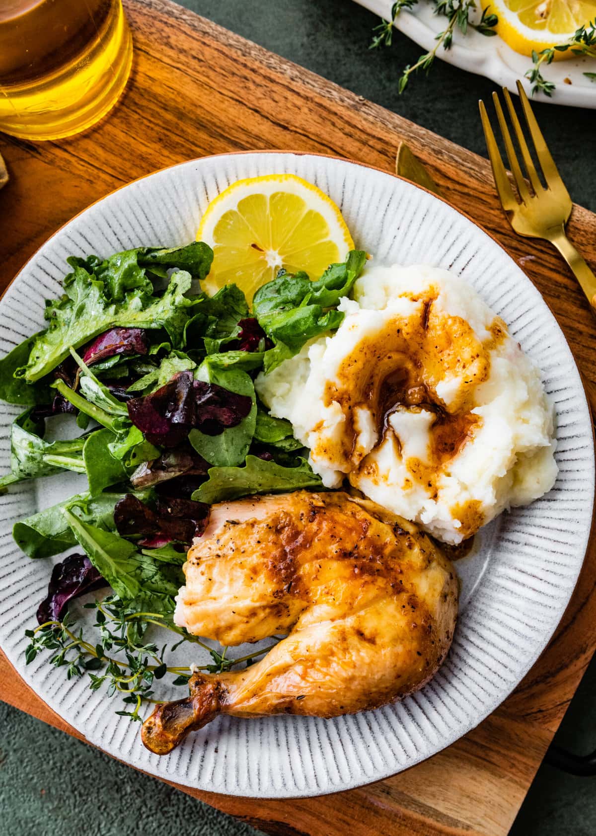Large piece of chicken thigh from the perfect roast chicken recipe on a plate with green salad, gravy, and mashed potatoes.