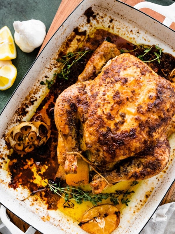 How Long to Cook Whole Chicken Recipe Perfect & Juicy- cooked roast chicken in a large roasting pan with lemons and garlic on the side.