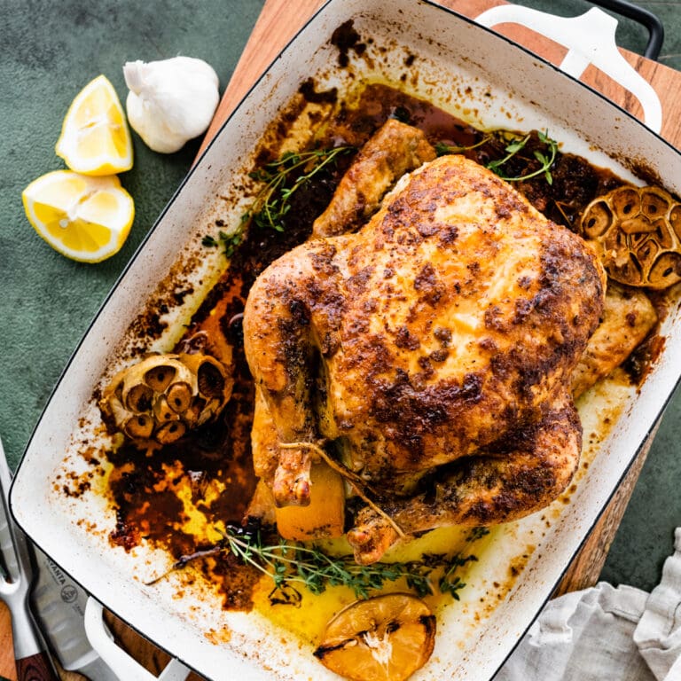 How Long to Cook Whole Chicken Recipe Perfect & Juicy- cooked roast chicken in a large roasting pan with lemons and garlic on the side.