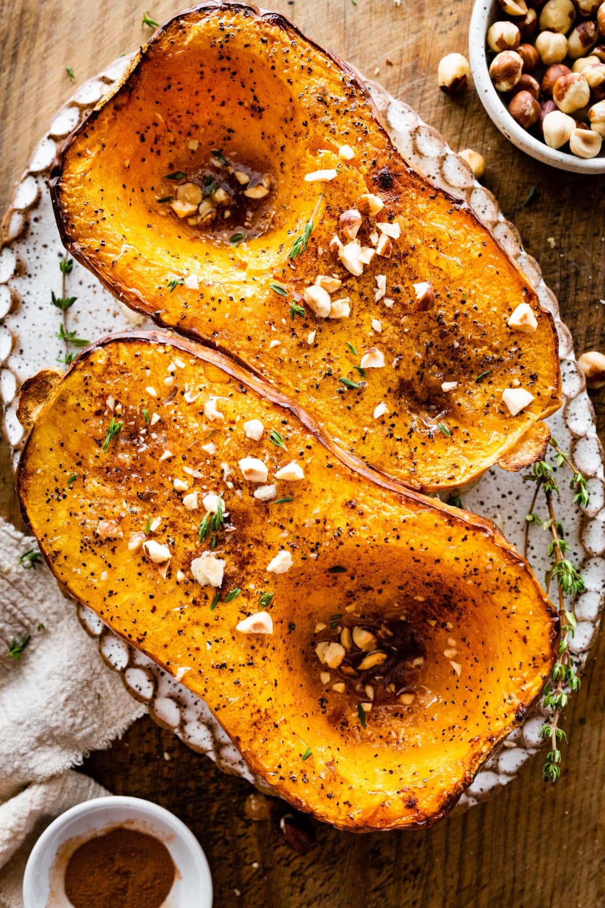 Baked butternut squash on a platter with nuts and herbs as seasoning. 