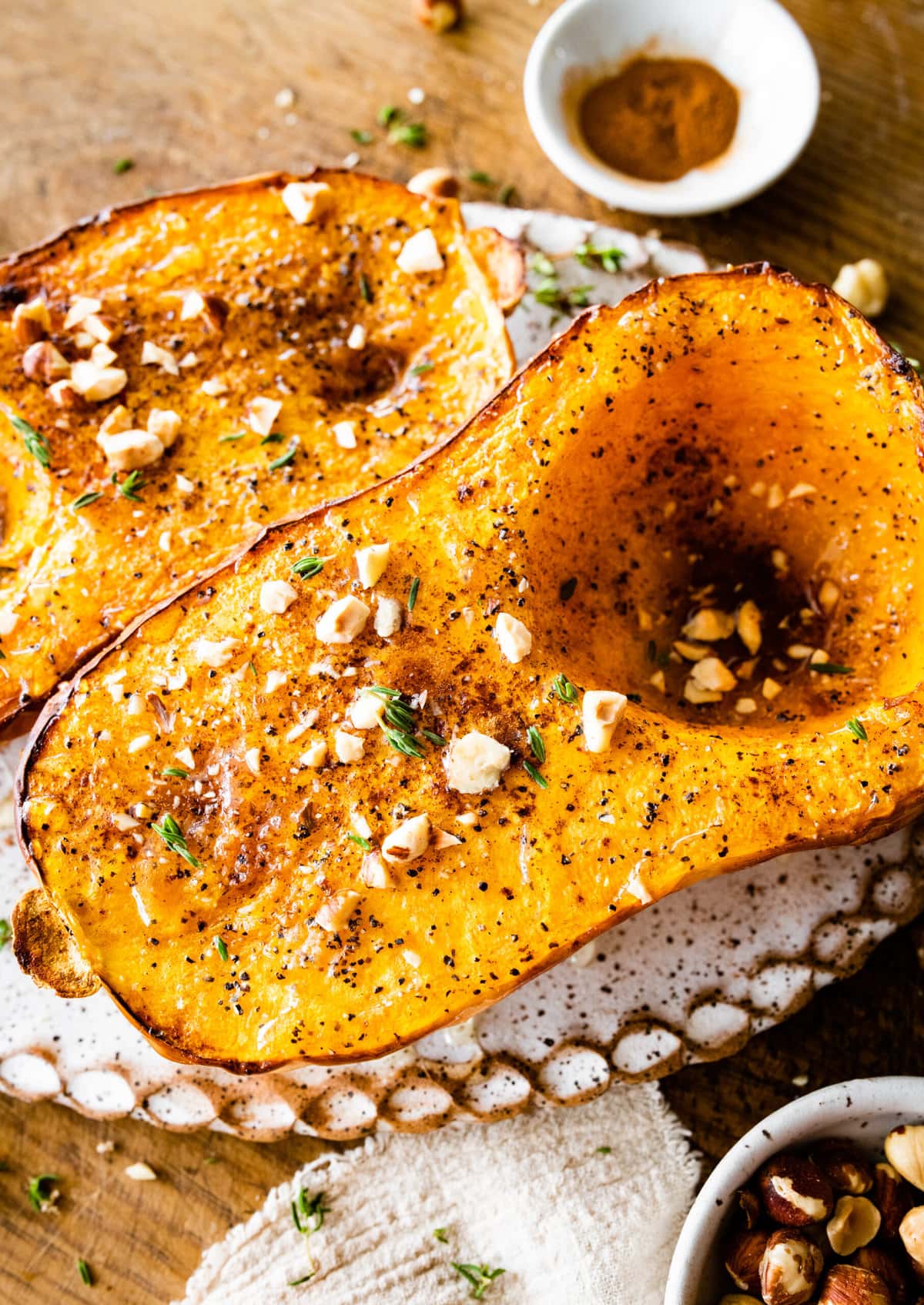 Baked butternut squash on a platter with nuts and herbs as seasoning.