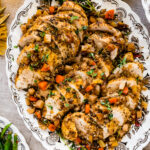 Beautiful sliced Juicy Oven Baked Chicken Breast Recipe on a serving platter with cooked veggies on top.