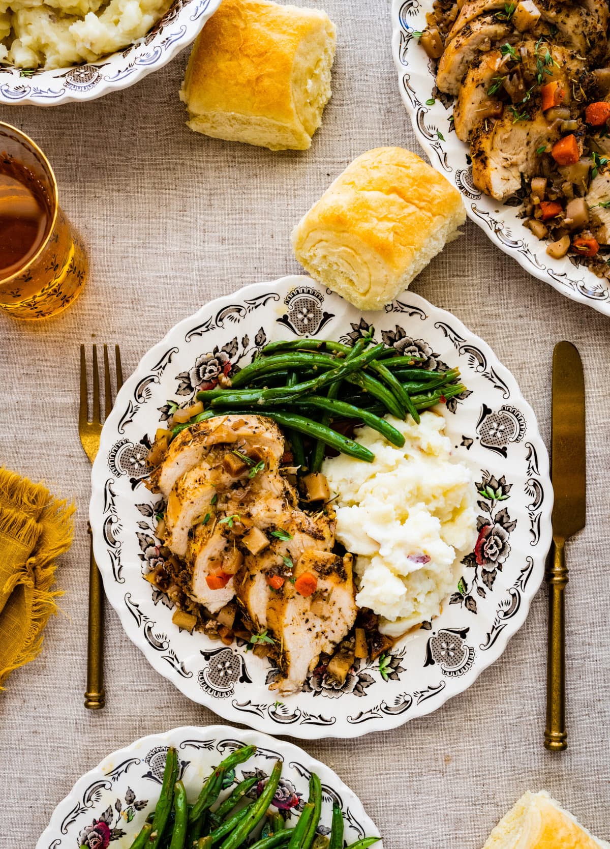 Juicy Oven Baked Chicken Breast Recipe on a plate with mashed potatoes and green beans and homemade rolls. beautiful table setting with silverware.