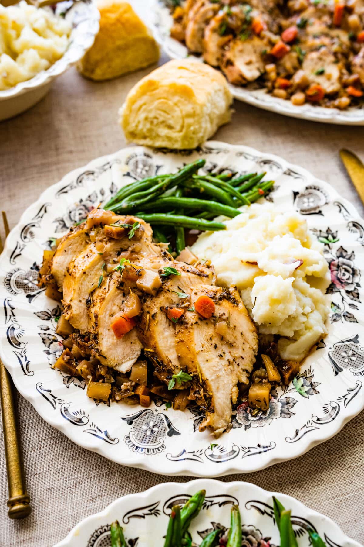 Juicy Oven Baked Chicken Breast Recipe on a plate with mashed potatoes and green beans and homemade rolls. beautiful table setting with silverware.