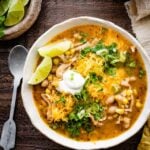 bowl of healthy white chicken chili with avocado, sour cream, lime, and cilantro as toppings. Chips in the bowl and on the side.