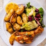 white plate with baked chicken drumstick with potatoes and salad.